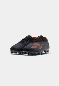 Black football boots with an intricate textured design, orange accents, and a low-cut shape. Fitted with black molded studs for traction.