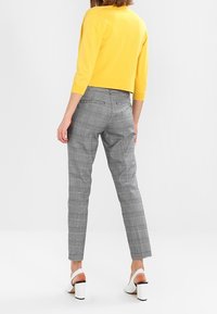 Geel cropped trui gecombineerd met grijze geruite broek. Witte sandalen met hak. Focus op casual stijl, aansluitend ontwerp en ruitpatroon.