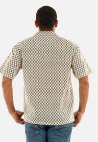 Camicia a maniche corte con motivo a quadretti, nei colori bianco e nero, realizzata in tessuto leggero, con vestibilità rilassata e colletto.