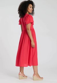 Röd midiklänning med korta puffärmar, texturerad tyg, åtsittande midja och svängd kjol; kombinerad med klara remmar på kilklackar.