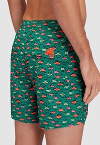 Costumi da bagno verde con un motivo colorato di pesci e onde, vita regolabile e tasca posteriore con chiusura a bottone.