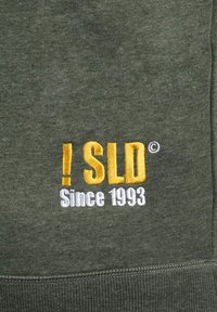 Dark green sweatshirt featuring embroidered text. Text in yellow reads "! SLD," followed by "Since 1993" in white. Soft, textured fabric.
