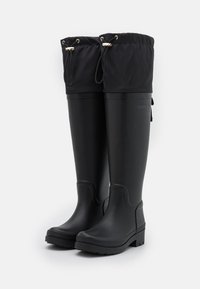 Bottes de pluie en caoutchouc noir avec un design haut, une semelle texturée, un haut à cordon de serrage et des accents en matériel doré. Finition lisse et construction robuste.