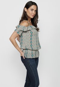 Top floreale scollato in tessuto leggero, con maniche volant, motivi turchesi e floreali, vita arricciata e design fluido.