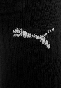 Logo de Puma blanco bordado en tejido ribeteado negro, probablemente parte de una prenda de ropa.