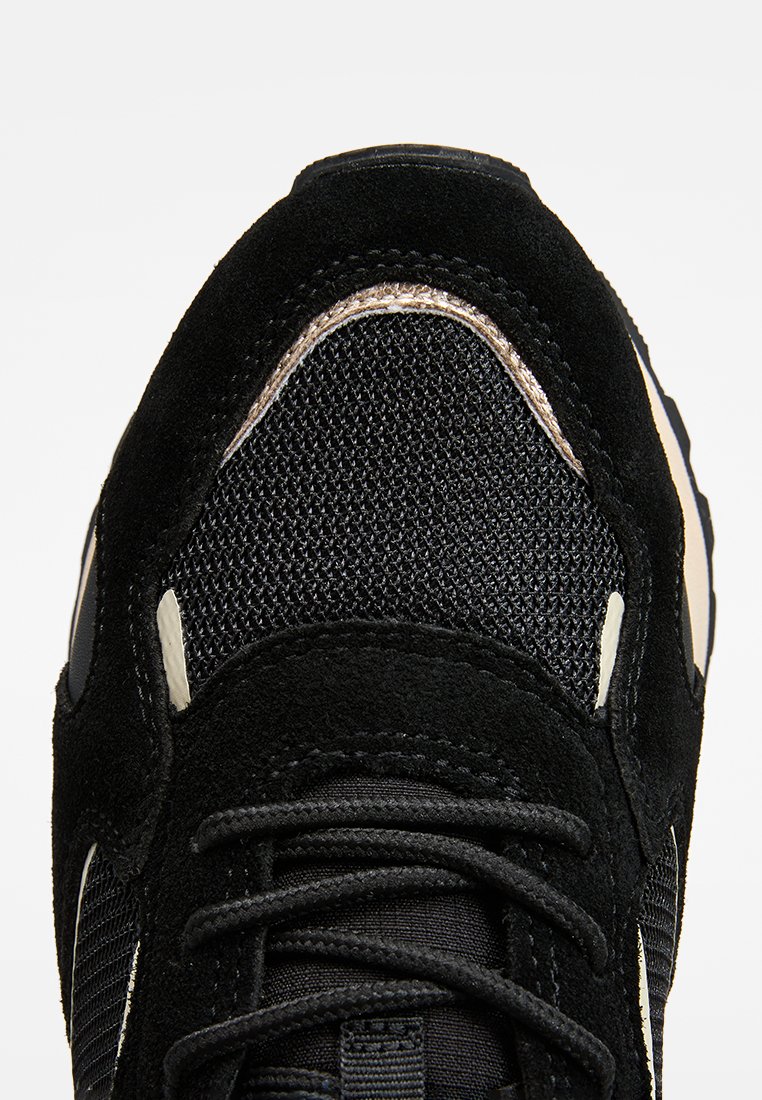 Zapatillas de ante negro y malla con parte superior texturizada, cordones negros planos y un acento metálico plateado a lo largo del diseño. Forma curva en la puntera.