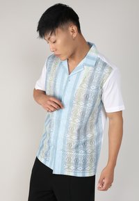 Chemise à manches courtes avec un motif bleu agrémenté de touches de vert et de noir, et un dos et des manches blancs unis.