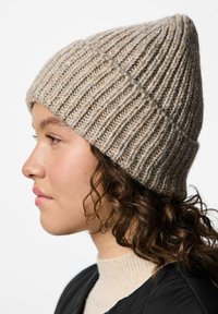 Berretto in maglia beige con punta. Presenta una texture a coste e un filato spesso, che migliora il calore e la vestibilità.