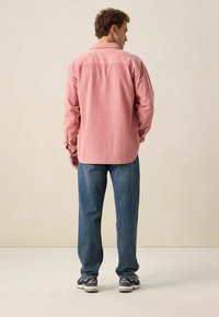Lange mouwen, lichtroze corduroy shirt met een rugpas, gecombineerd met losse blauwe jeans en grijze sportschoenen met accenten.