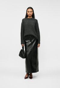 Γκρί, υφασμάτινος πλεκτός πουλόβερ με φαρδιές μανσέτες, σε συνδυασμό με μαύρη δερμάτινη φούστα μέχρι τον αστράγαλο. Συνδυασμένο με μικρή μαύρη τσάντα και μπορντό ψηλοτάκουνα.