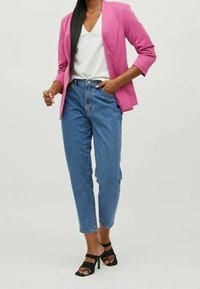 Růžový tailorovaný blejzr přes bílý top s výstřihem do V, doplněný světlými modrými džíny s vysokým pasem a černými sandály na podpatku.