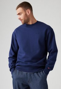 Navyblauwe sweatshirt van katoen, met een ronde hals, geribbelde mouwen en een reliëflogo op de borst, gecombineerd met denim broek.