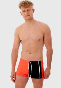 Shorts de bain pour hommes avec un devant orange vif et un dos noir, ornés d'une bande blanche et d'une taille élastique avec cordon de serrage. Tissu lisse, conception ajustée.