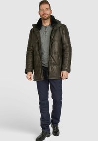 Dunkles Leder-Puffermantel mit einem schwarzen, mit Fell gefütterten Kragen, graues Henley-Shirt und dunkle Jeans, ergänzt durch schwarze Dressschuhe.