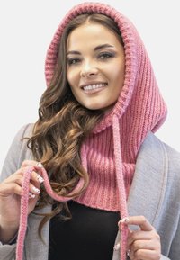 Cappuccio lavorato a maglia rosa con texture a coste, dotato di lunghe legature e una vestibilità aderente attorno al collo, indossato sopra un cappotto grigio.