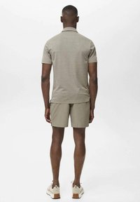 Polo shirt da uomo a maniche corte, di colore khaki, con un motivo testurizzato, abbinato a pantaloni corti khaki e sneakers chiare.