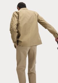 Khaki jas met een kraag, enkele rugnaad en knoopmanchetten, gecombineerd met bijpassende khaki broek. Gladde katoenen stof.