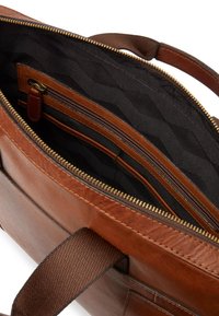 Brun läderväska med dragkedjestängning, med ett svart geometriskt mönstrat foder och flera inre fickor, inklusive en ficka med dragkedja.