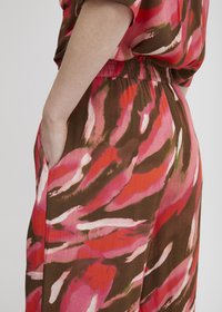 Svetlo obarvan kombinezon s vrtnim pink in rjavim vzorcem, ki ima sproščen kroj, elastičen pas in stranske žepe.