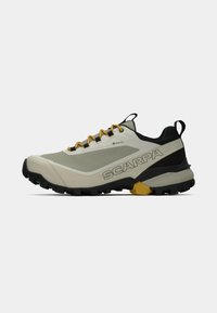 Zapato de trail gris claro y negro con acentos amarillos. Hecho de un material texturizado, con una suela resistente y un logo en el lateral.