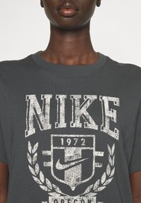 T-shirt en coton gris avec un imprimé bold et usé en blanc "NIKE 1972" et un logo avec des accents de feuilles, col rond et manches courtes.