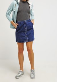 Gonna di jeans con bottoni sul davanti, due tasche e orlo grezzo. Abbinata a una maglietta grigia e sneaker argentate. Felpa azzurra indossata.