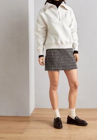 Bílý texturovaný pulovr s půlzipem, doplněný černobílou vzorovanou mini sukní. Černé loafers a smetanové kotníkové ponožky dotv�ářejí celý vzhled.