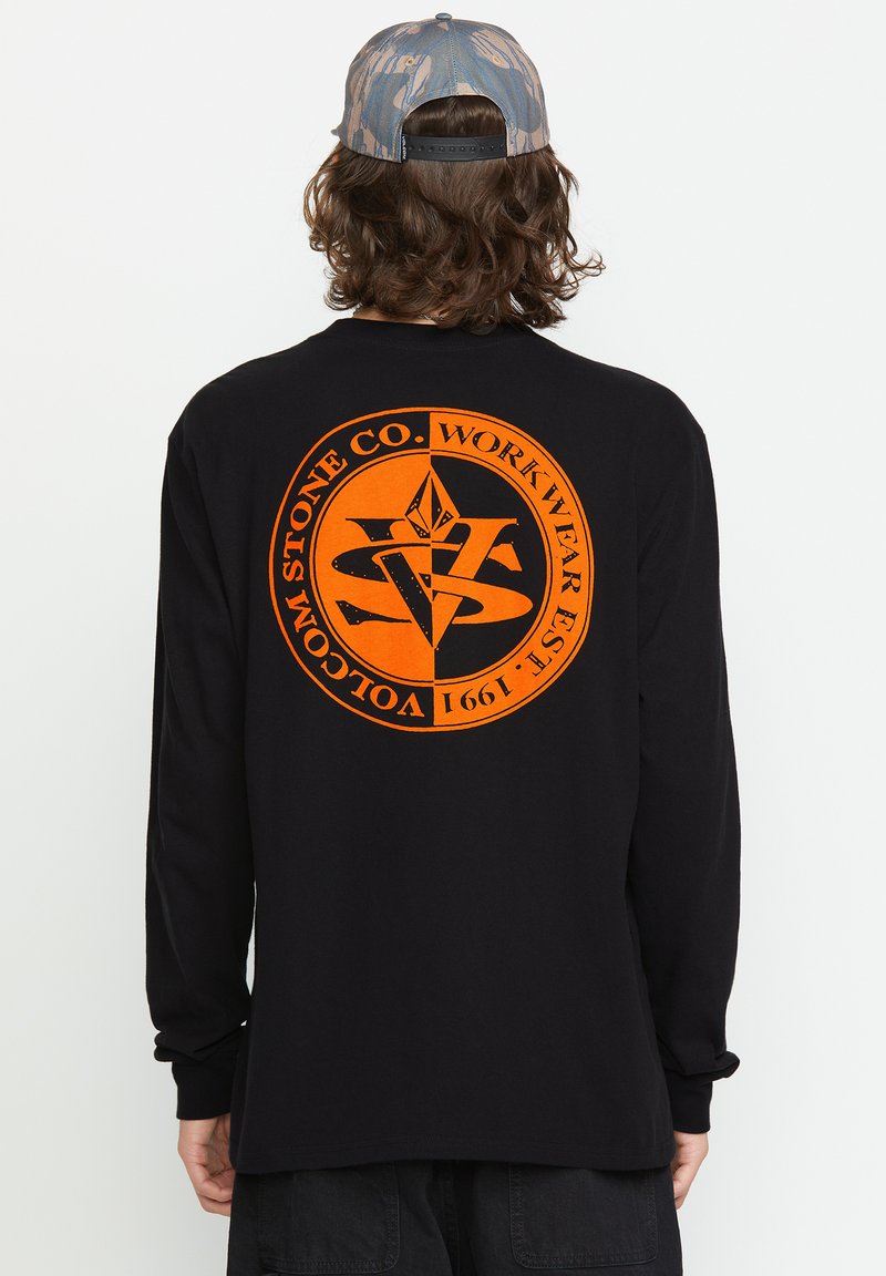 Schwarzes Langarmshirt mit einem großen orangen kreisförmigen Grafik und Text auf der Rückseite. Das Design beinhaltet geometrische Formen und ein Logo.