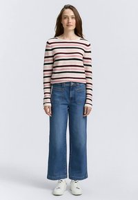 Pasiasta bluzka z długim rękawem w kremowym, bordowym i czarnym kolorze zestawiona z szerokimi niebieskimi dżinsami. Białe trampki dopełniają strój.