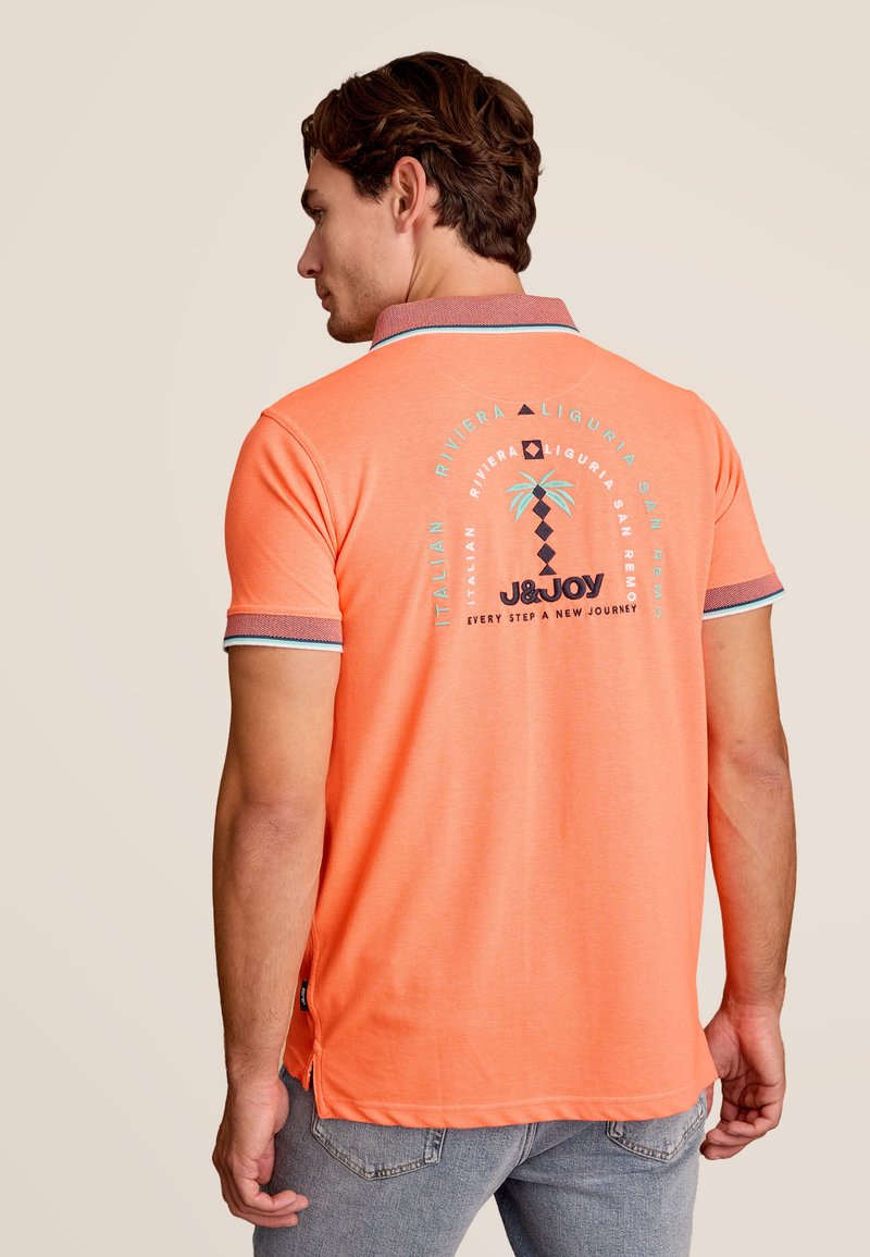 Oranje poloshirt met contrasterende kraagdetails en palmmotief. Bevat het "J&JOY" logo en tekst op de achterkant, gemaakt van zachte stof.