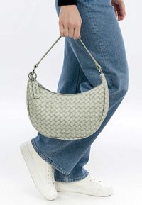 Borsa hobo di colore grigio chiaro con un motivo geometrico, dotata di chiusura a zip e sottile tracolla, tenuta da una persona che indossa denim.