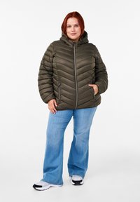 Olivgrön puffjacka med huva, som har en chevron-quiltad design, blixtlåsfickor och en främre blixtlåsdragning. Matchas med blå jeans.