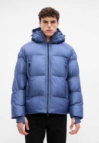 Giacca puffa blu, con zip frontale, cappuccio a doppio strato e due tasche con zip. Realizzata in tessuto liscio e isolato con texture trapuntata.