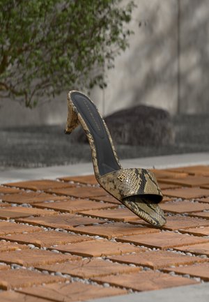 High-Heeled Mule-Schuh mit Schlangenmuster und goldenem Logo, der auf einer strukturierten Holzoberfläche im Freien ruht.