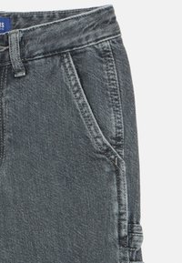 Tumed hallid teksapüksid, millel on tekstuuriga viimistlus, küljetaskud ning kontrastne õmblus vöökoha ja taskute ääres.