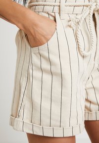 Béžové proužkované šortky z texturované látky, s bočními kapsami a zavazovacím pasem se zauzlovanou šňůrkou, s obrácenými lemy.