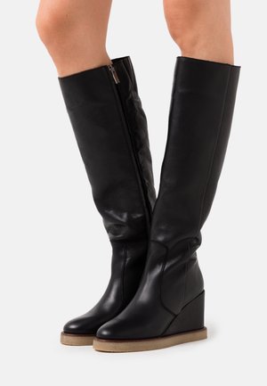 Bottes à semelle compensée en cuir noir montant jusqu'aux genoux, avec une texture lisse, une fermeture éclair latérale et un design incurvé subtil sur le talon compensé.