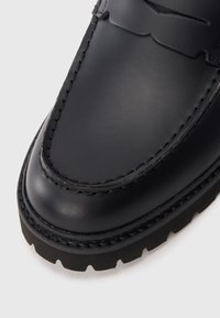 Fekete bőr loaferek varrott részletezéssel, kerek orral és texturált talppal. Simaságot és fényes felületet kínálnak, minimalista design kiegészítőkkel.