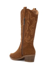 Botas de vaquero de ante marrón altas con un patrón decorativo, cremallera lateral y un tacón bajo apilado. Superficie texturizada y detalles de costura curvada.