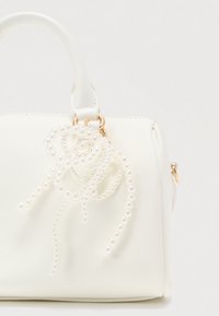 Λευκή τσάντα χειρός με υφή στην επιφάνεια, διακοσμημένη με μαργαριταρένια λεπτομέρεια, χρυσά μεταλλικά στοιχεία και δομημένο σχήμα.