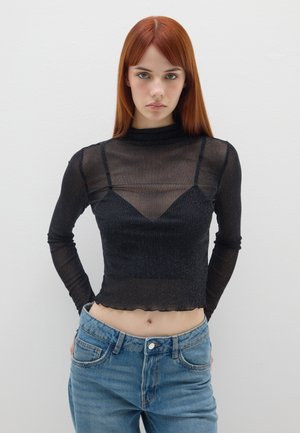 Top noir transparent à manches longues avec un col montant et une coupe ajustée. Comprend une sous-couche triangulaire et des bords bruts. Associé à un jean bleu taille haute.