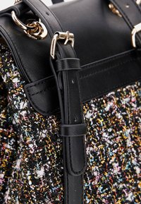 Cintura in pelle nera con fibbia dorata attaccata a una borsa in tessuto multicolore e testurizzato, con fili intrecciati e accenti metallici.