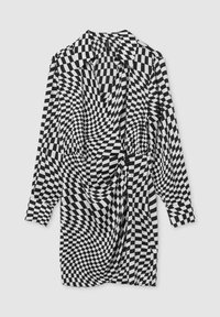 Abito a scacchi bianco e nero con scollatura profonda, maniche lunghe e un design in tessuto intrecciato che crea un effetto ottico distorto.