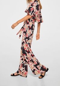 Květinový overálek v černé, béžové a červené barvě; má široké rukávy, páskový pas a volný, splývavý střih. Nosený s černými sandály.