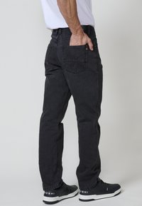 Vaqueros de mezclilla negra con un corte recto, diseño de cinco bolsillos y detalles de costura sutiles. Combinados con zapatillas negras con acentos blancos.