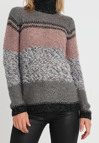 Stickad tröja med hög krage, prydd med horisontella ränder i rosa, grått och svart. Strukturerad tyg med avslappnad passform och ribbade kanter.