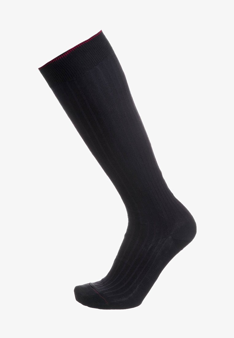 Calza nera fino al ginocchio con texture a coste e sottile bordo rosso nella parte superiore e nella punta, mostrata su uno sfondo bianco.