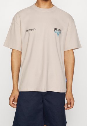 Beige katoenen T-shirt met korte mouwen, voorzien van een frontprint met de tekst "ONE RIDE TO HEAVEN" en een blauw abstract ontwerp. Label aan de linkerkant.