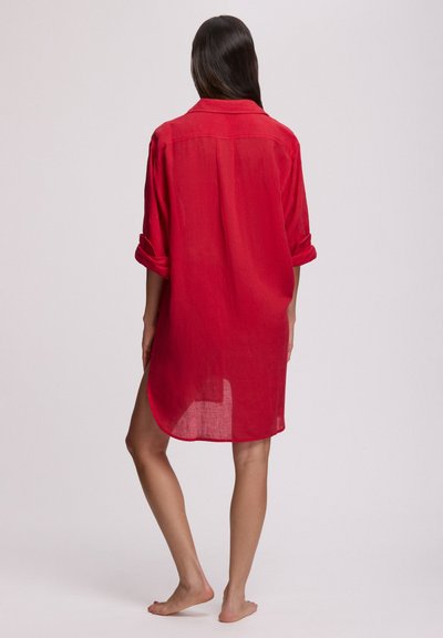 Κόκκινο φόρεμα από λινό με μανίκια που ρυθμίζονται με ρολά, γιακά και καμπυλωτή γραμμή στο κάτω μέρος, αναδεικνύοντας μια ελαφριά, ημιδιάφανη υφή.