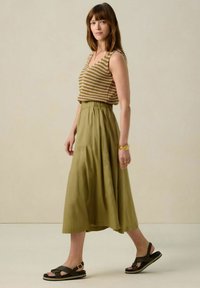 Haut sans manches rayé marron et vert avec un décolleté en V, associé à une jupe fluide verte olive et des sandales noires avec un détail de boucle.